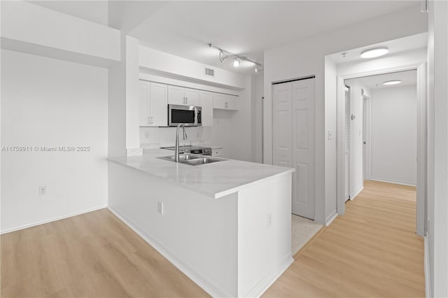 kitchen featuring light wood finished floors, stainless steel microwave, light countertops, a peninsula, and a sink