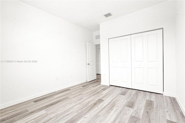 unfurnished bedroom with a closet, visible vents, light wood-type flooring, and baseboards