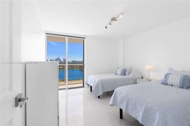 bedroom with rail lighting, a water view, light tile patterned floors, and expansive windows