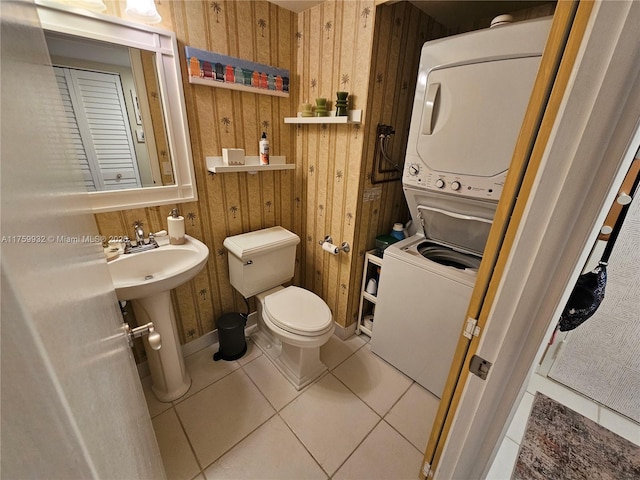 bathroom with wooden walls, a sink, tile patterned flooring, stacked washer and dryer, and toilet