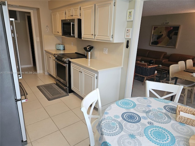 kitchen featuring a textured ceiling, open floor plan, appliances with stainless steel finishes, light countertops, and light tile patterned floors