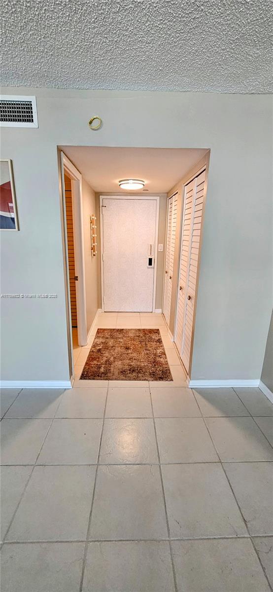 corridor with light tile patterned floors, visible vents, a textured ceiling, and baseboards