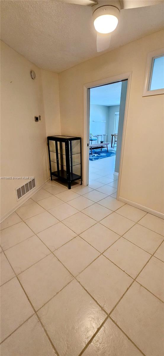 hallway with light tile patterned flooring, visible vents, a textured ceiling, and baseboards