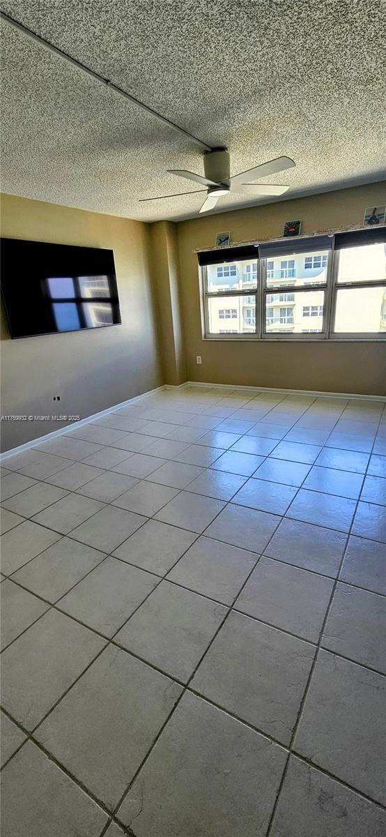 tiled empty room with baseboards, a textured ceiling, and a ceiling fan