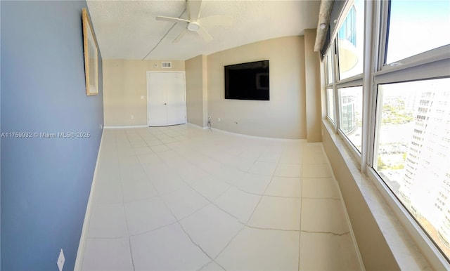 empty room with a textured ceiling, light tile patterned floors, baseboards, and ceiling fan