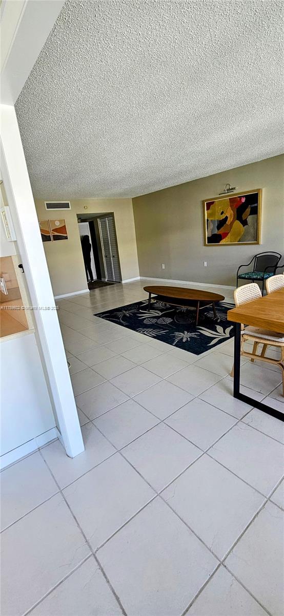 living area with light tile patterned flooring, baseboards, visible vents, and a textured ceiling