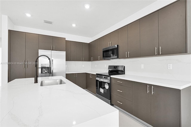 kitchen with visible vents, a sink, light stone counters, appliances with stainless steel finishes, and dark brown cabinets