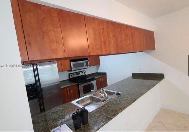 1200 Brickell Bay Dr Unit 3318, Miami, FL 33131 - kitchen with appliances with stainless steel finishes, a sink, brown cabinets, light tile patterned flooring, and dark stone counters