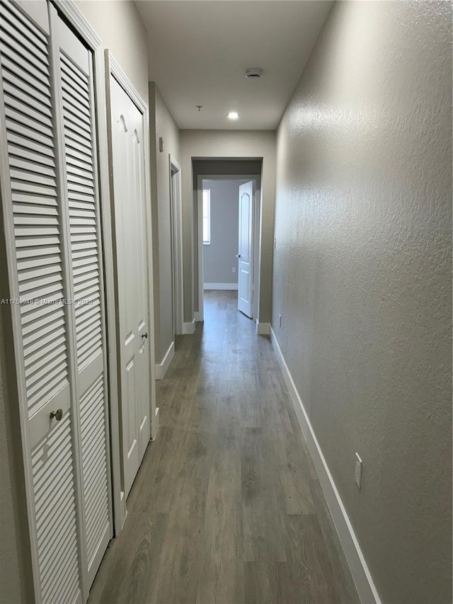 hall with a textured wall, baseboards, and wood finished floors