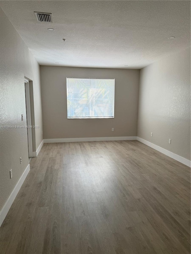 spare room with visible vents, baseboards, a textured ceiling, and wood finished floors