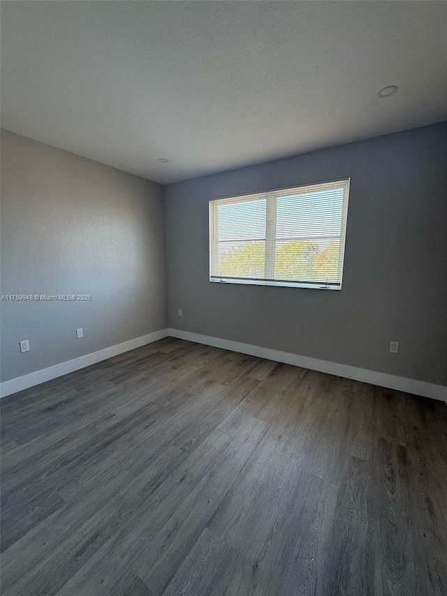 spare room featuring baseboards and dark wood-style flooring