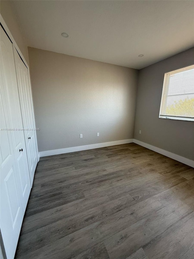 unfurnished bedroom featuring baseboards, dark wood-style flooring, and a closet