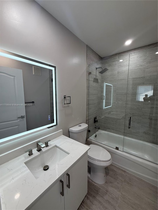 bathroom with visible vents, vanity, toilet, and bath / shower combo with glass door