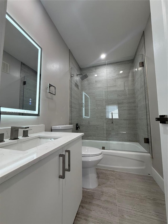 bathroom with visible vents, baseboards, toilet, combined bath / shower with glass door, and vanity