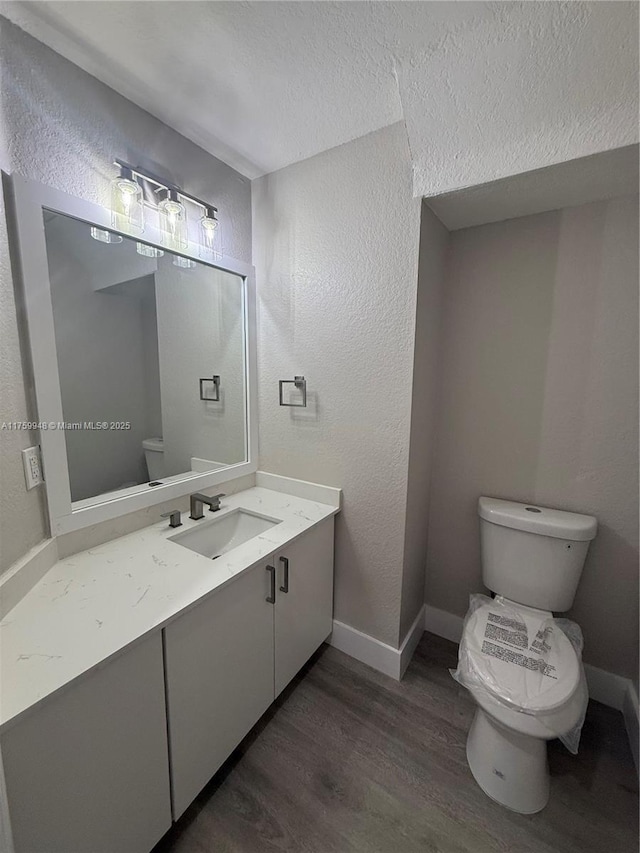 bathroom with a textured wall, toilet, baseboards, and wood finished floors