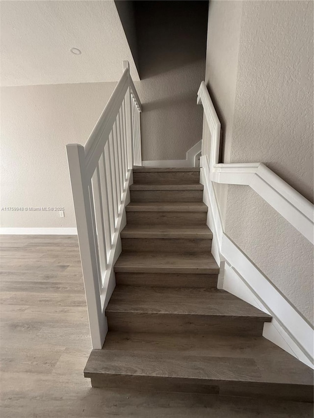 stairs featuring wood finished floors, baseboards, and a textured wall