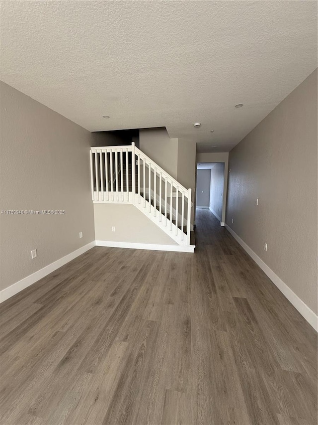 spare room featuring stairs, wood finished floors, baseboards, and a textured ceiling