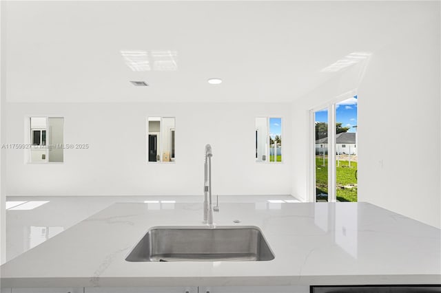 kitchen with light stone counters, visible vents, recessed lighting, and a sink