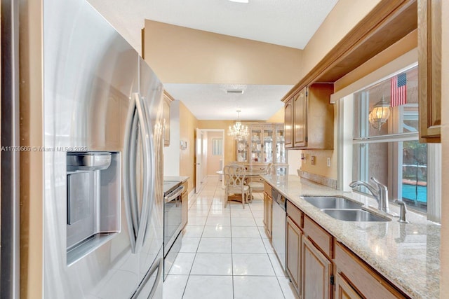 kitchen featuring a sink, decorative light fixtures, light stone counters, appliances with stainless steel finishes, and light tile patterned flooring