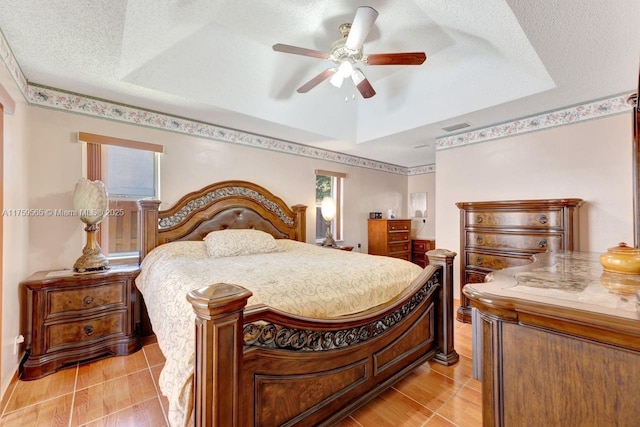 bedroom featuring visible vents, a raised ceiling, a textured ceiling, and ceiling fan