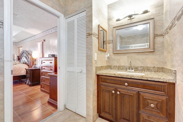 ensuite bathroom with ensuite bathroom, a textured ceiling, a closet, tile walls, and vanity