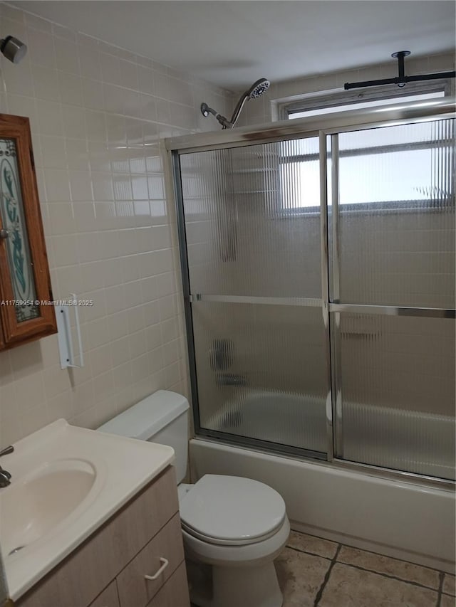 full bath with tile patterned floors, toilet, combined bath / shower with glass door, tile walls, and vanity