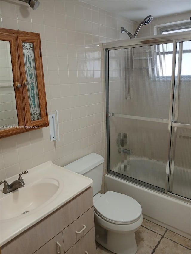 full bathroom with vanity, bath / shower combo with glass door, tile patterned flooring, tile walls, and toilet