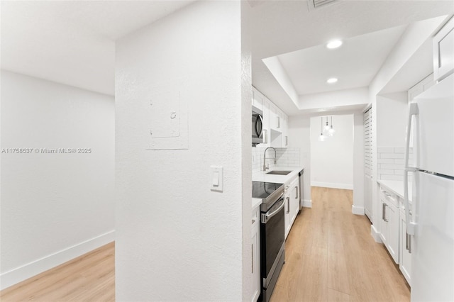 kitchen featuring light wood-type flooring, a sink, backsplash, appliances with stainless steel finishes, and baseboards