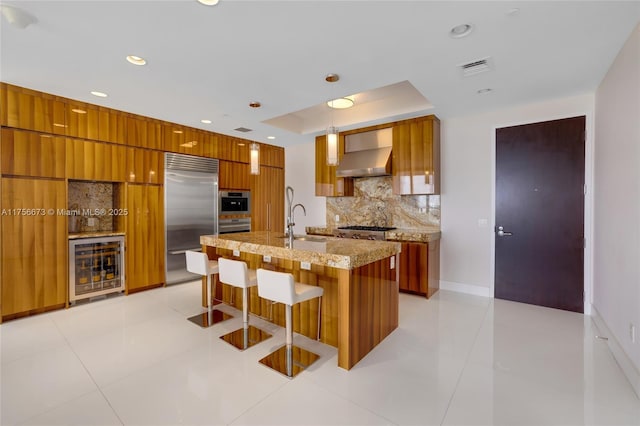 kitchen featuring stainless steel appliances, brown cabinets, modern cabinets, and wall chimney range hood