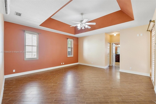 empty room featuring a tray ceiling, wood finished floors, visible vents, and ceiling fan