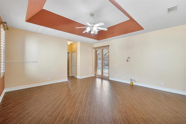 empty room with visible vents, a raised ceiling, baseboards, and dark wood finished floors