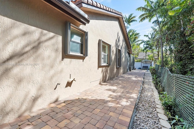 view of side of home featuring stucco siding, a patio area, and fence