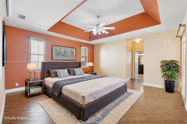 bedroom with a tray ceiling, multiple windows, visible vents, and wood tiled floor