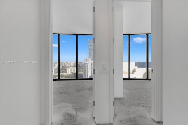 empty room with a view of city, floor to ceiling windows, unfinished concrete flooring, and a healthy amount of sunlight