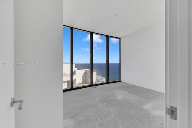 spare room featuring concrete floors, a wall of windows, and a water view