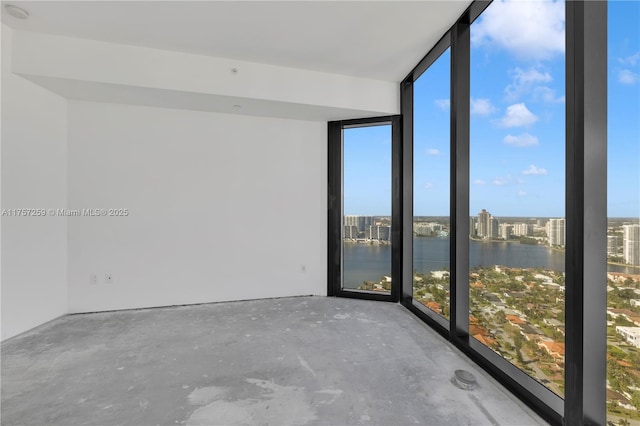 unfurnished room with a wall of windows, a water view, and concrete flooring