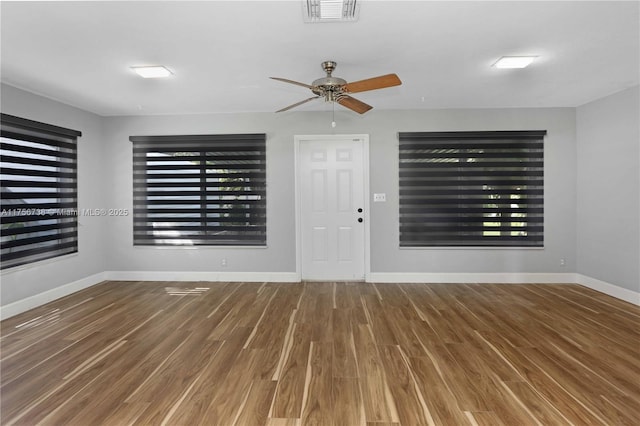 empty room with wood finished floors, visible vents, and baseboards