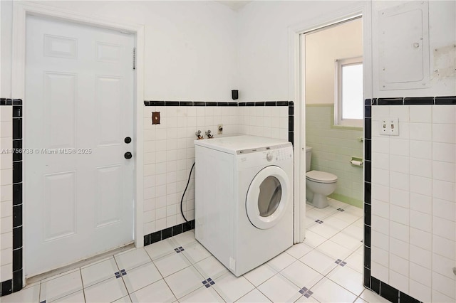 laundry area with light tile patterned floors, electric panel, washer / dryer, wainscoting, and tile walls