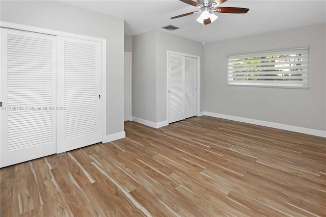 unfurnished bedroom featuring multiple closets, wood finished floors, visible vents, and baseboards