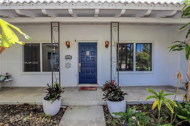 doorway to property with stucco siding, a porch, and a tile roof