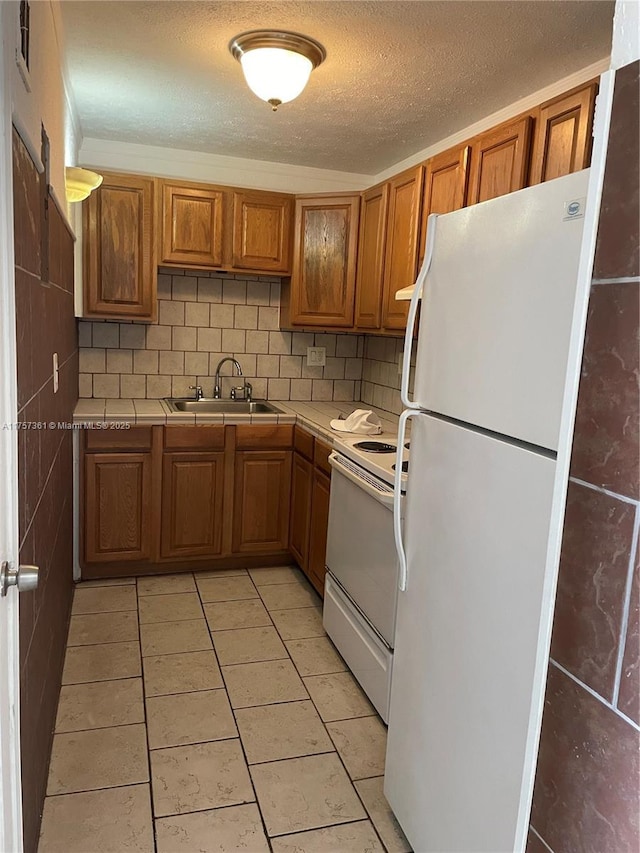 kitchen featuring white appliances, tile countertops, a sink, decorative backsplash, and brown cabinets