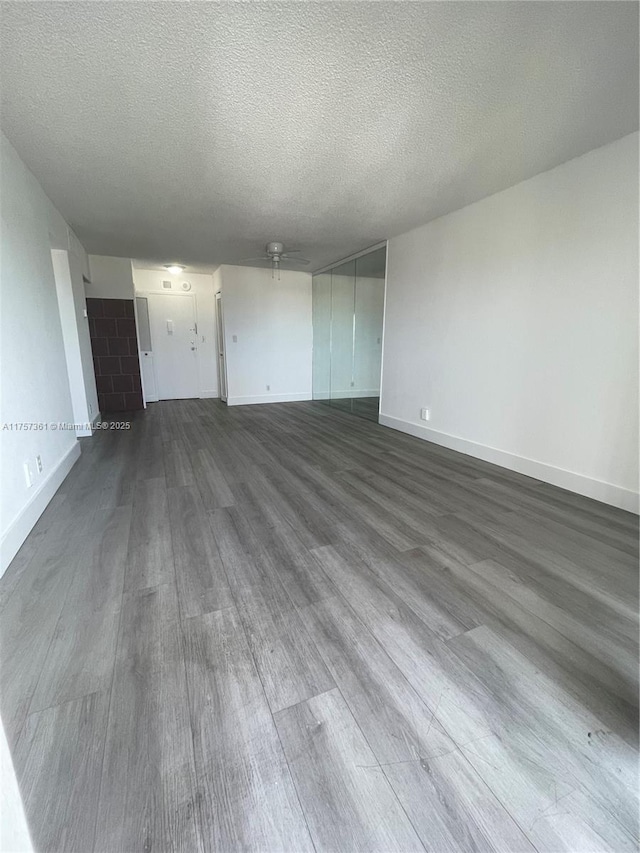 unfurnished living room with dark wood-style floors, a textured ceiling, and baseboards