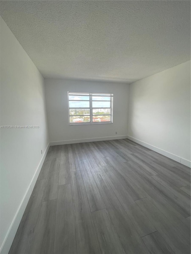 unfurnished room featuring baseboards, a textured ceiling, and dark wood-style floors