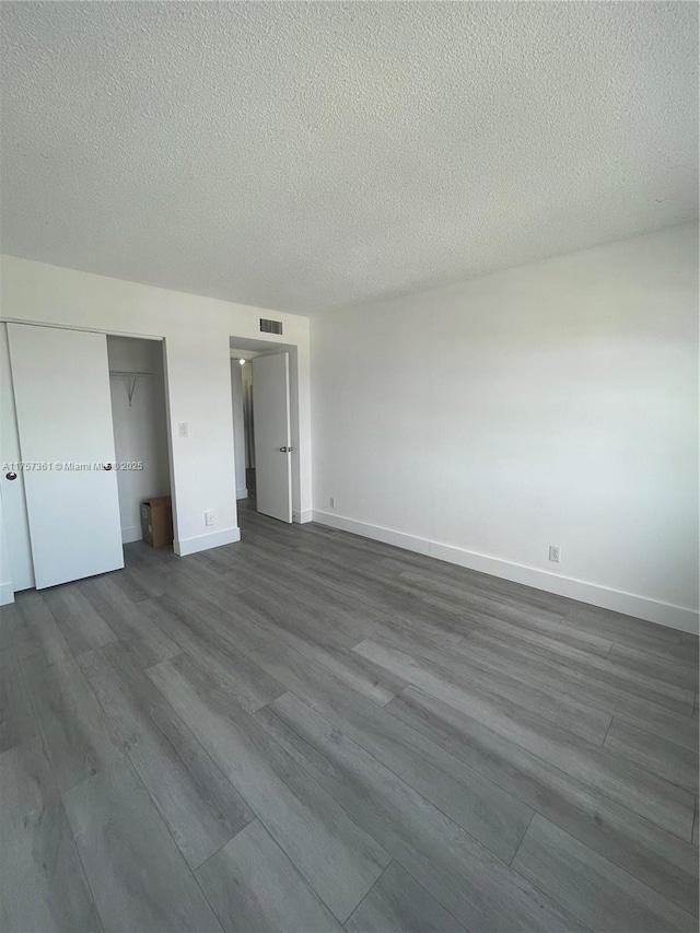 unfurnished bedroom with dark wood-style floors, visible vents, baseboards, a closet, and a textured ceiling