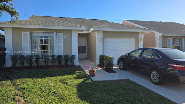 ranch-style house featuring a shingled roof, concrete driveway, a front yard, stucco siding, and an attached garage