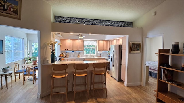 kitchen with light brown cabinets, tasteful backsplash, stainless steel fridge, a peninsula, and light countertops