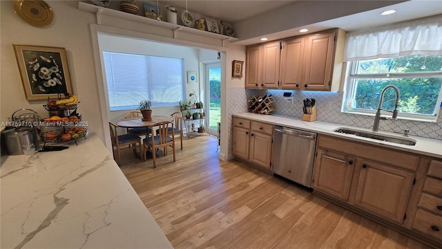 kitchen with dishwasher, light stone counters, decorative backsplash, light wood-style flooring, and a sink