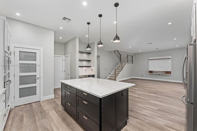 kitchen with light wood-type flooring, visible vents, a center island, stainless steel appliances, and dark cabinets