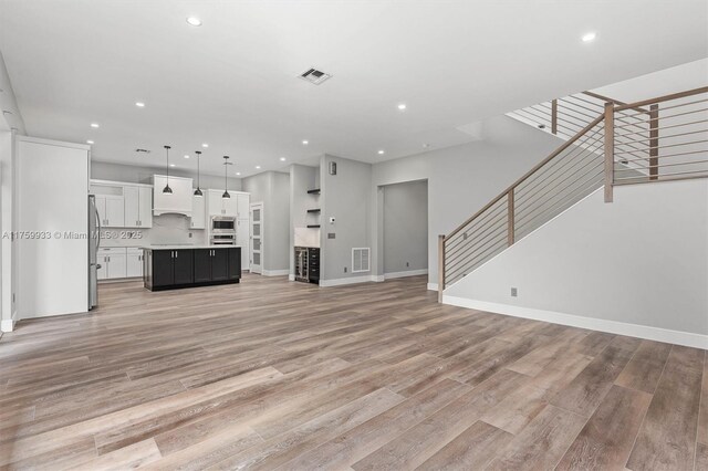 unfurnished living room featuring stairs, light wood-style flooring, and visible vents