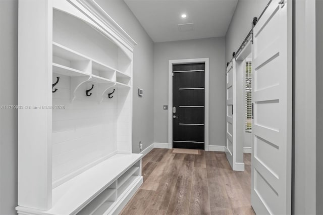 mudroom with a barn door, wood finished floors, and baseboards